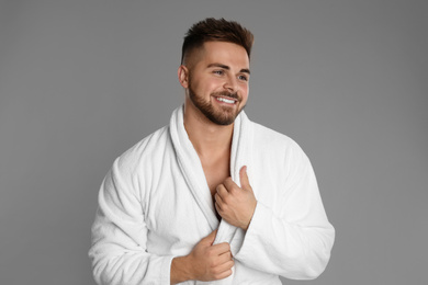 Happy young man in bathrobe on grey background