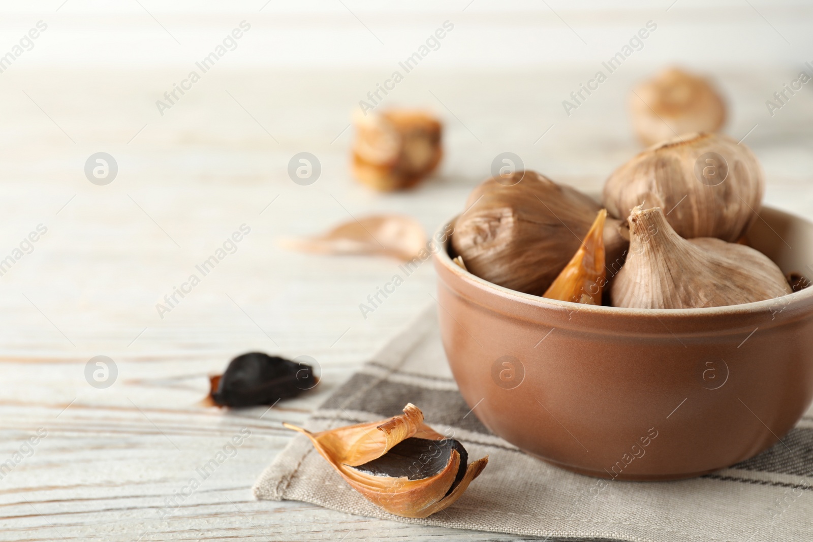 Photo of Bowl and black garlic on white wooden table. Space for text