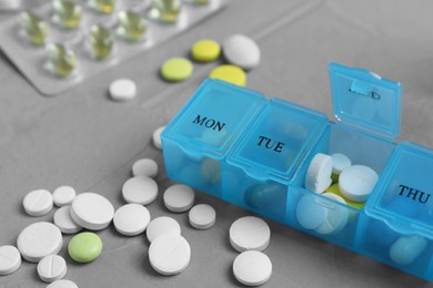 Photo of Weekly pill box with medicaments on grey table, closeup