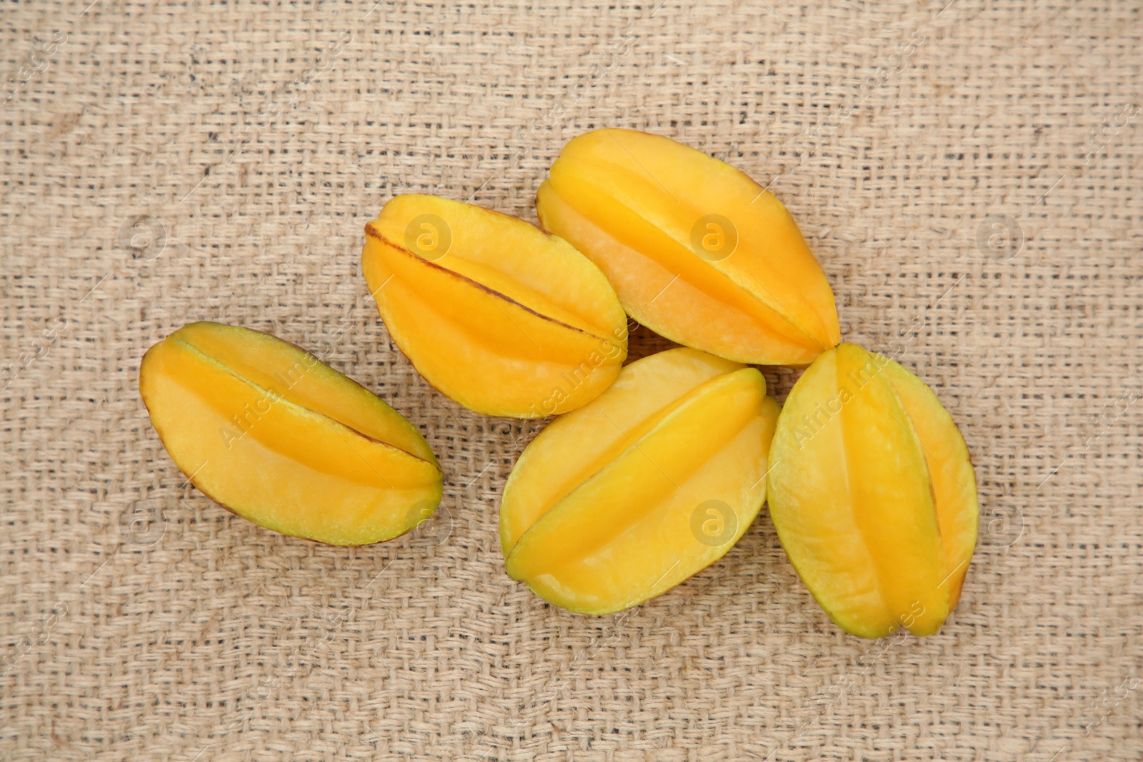 Photo of Delicious ripe carambolas on burlap fabric, flat lay