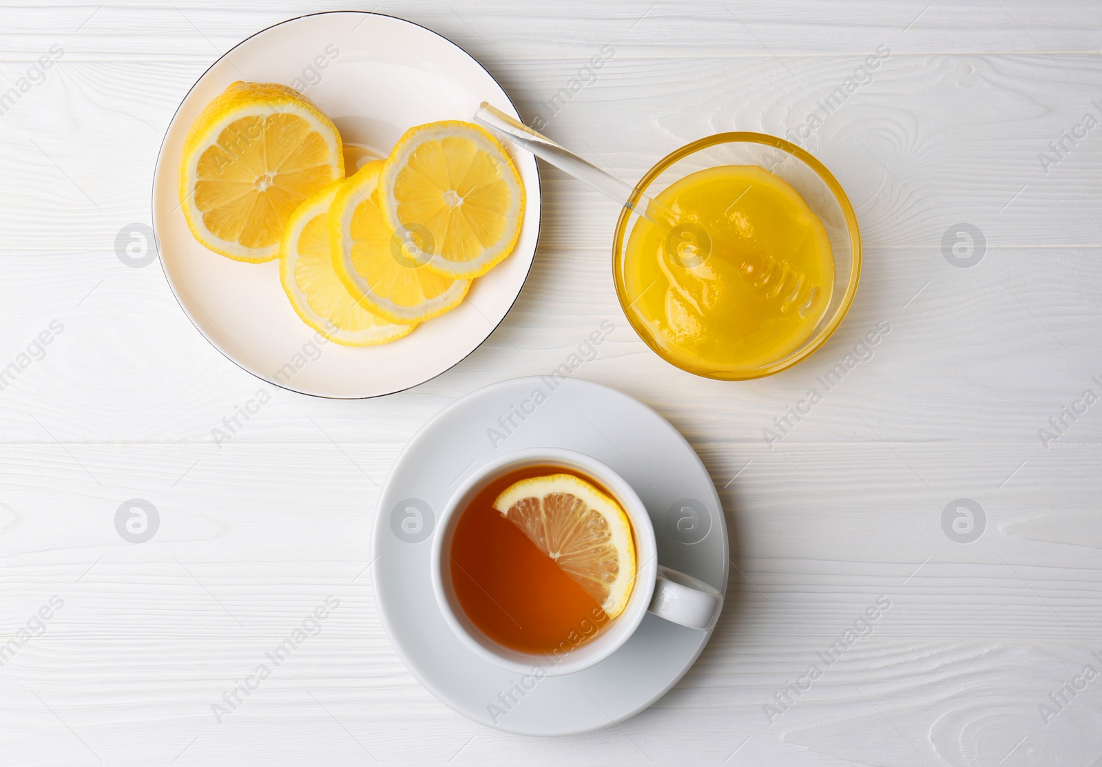 Photo of Cup with delicious immunity boosting tea, lemon and honey on white wooden table, flat lay