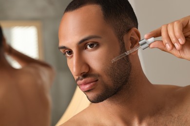 Photo of Handsome man applying cosmetic serum onto face indoors, closeup. Space for text