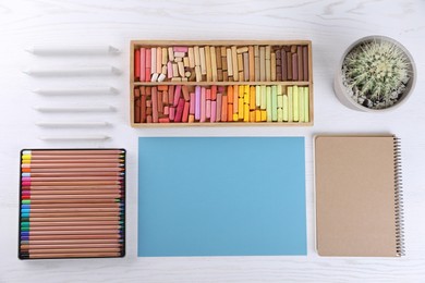 Photo of Layout with blank paper, soft pastels and other drawing supplies on white wooden table at artist's workplace, top view. Space for design