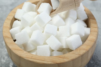 White sugar cubes in wooden bowl and scoop on grey table, closeup
