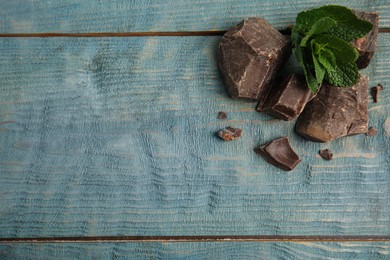 Tasty dark chocolate pieces with mint on blue wooden table, flat lay. Space for text