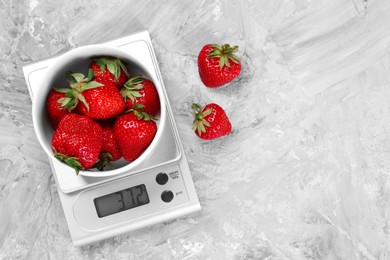 Photo of Kitchen scale with bowl of strawberries on grey textured table, flat lay. Space for text