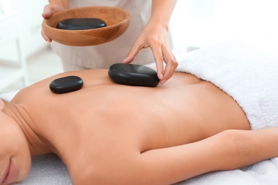 Photo of Beautiful young woman getting hot stone massage in spa salon