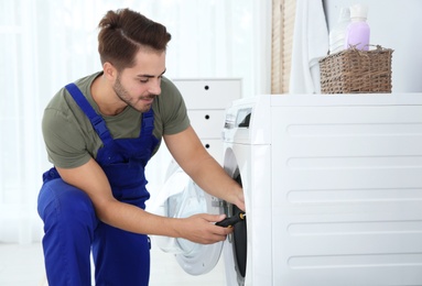 Photo of Young handyman fixing washing machine at home. Laundry day