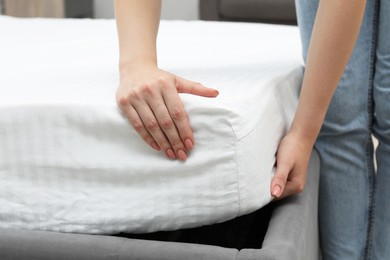 Photo of Woman putting new soft mattress on bed indoors, closeup