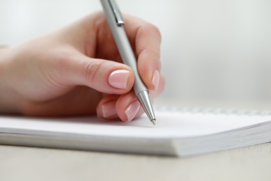 Photo of Woman writing in notebook at wooden table, closeup