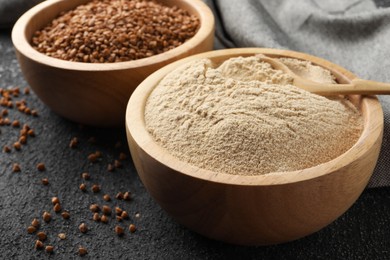 Photo of Buckwheat flour and grains in bowls on black table, closeup