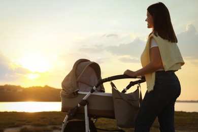 Happy mother with baby in stroller walking near river at sunset