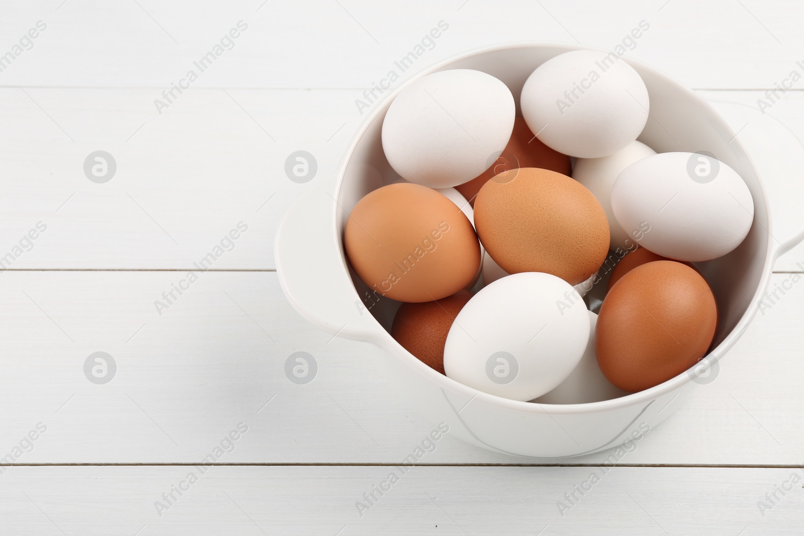 Photo of Unpeeled boiled eggs in saucepan on white wooden table. Space for text