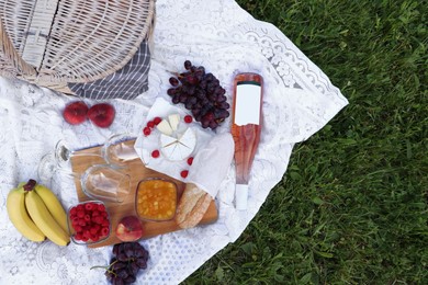 Photo of Picnic blanket with tasty food, basket and cider on green grass outdoors, flat lay