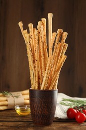 Photo of Delicious grissini sticks, oil, rosemary and tomatoes on wooden table