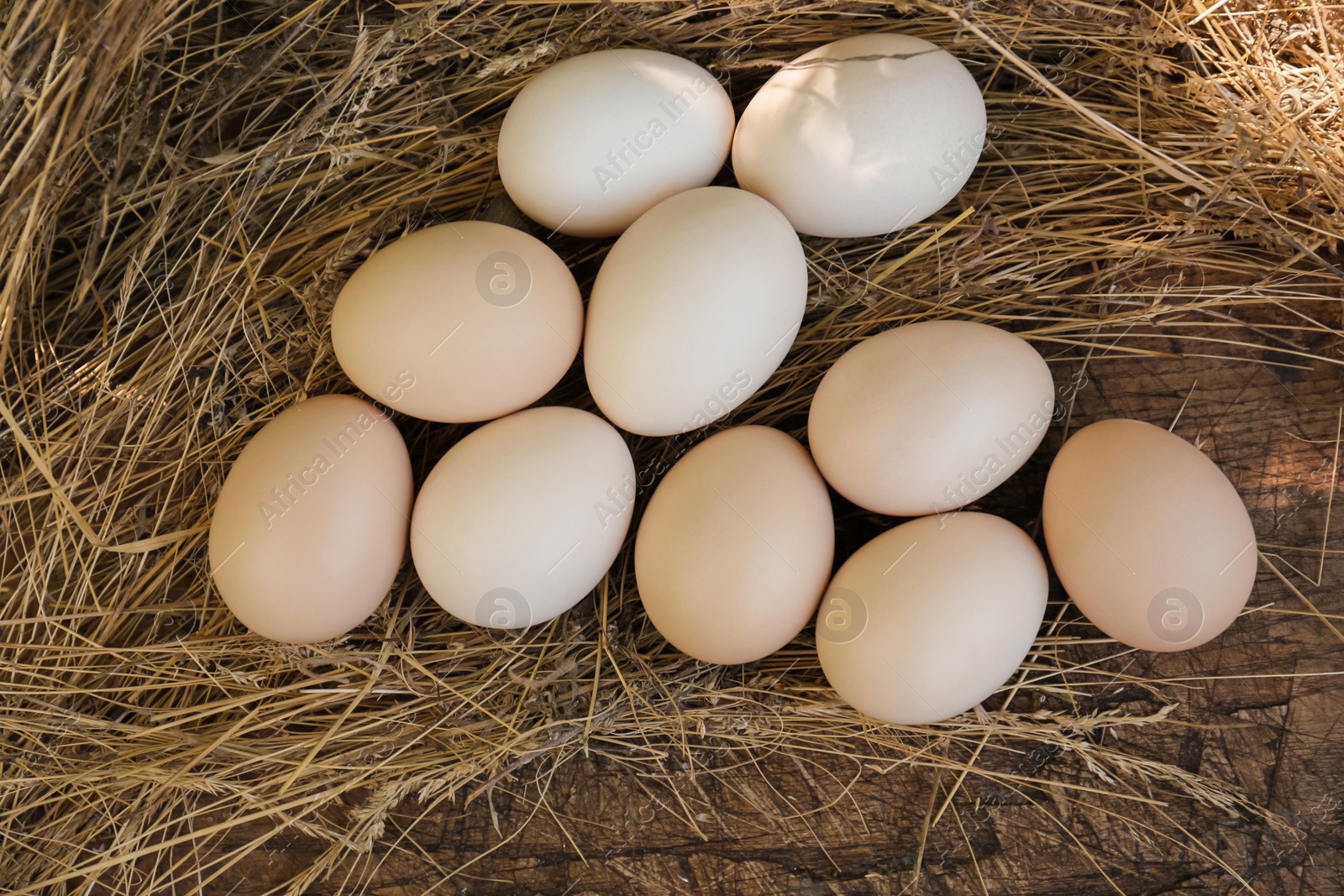 Photo of Fresh raw eggs and straw on wooden surface, flat lay