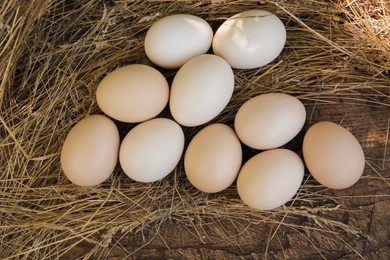 Fresh raw eggs and straw on wooden surface, flat lay