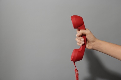 Photo of Closeup view of woman holding red corded telephone handset on light grey background, space for text. Hotline concept