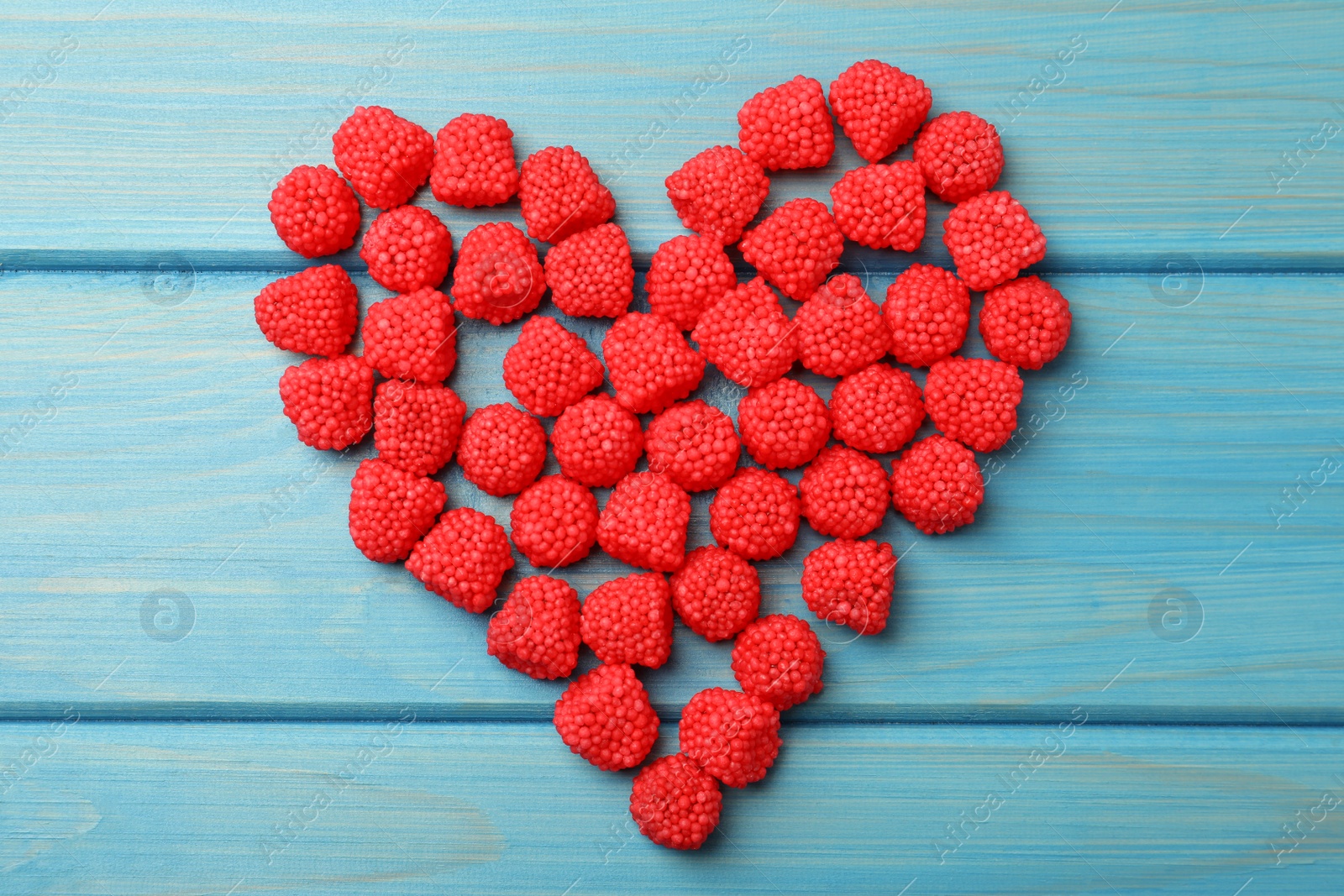 Photo of Heart made of delicious gummy raspberry candies on light blue wooden table, flat lay