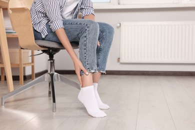 Photo of Woman suffering from leg pain on chair at home, closeup