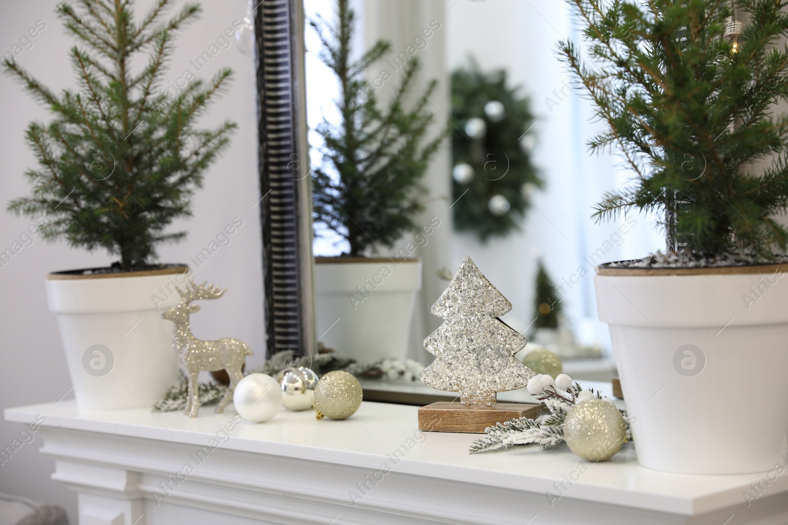 Photo of Little fir trees and Christmas decorations on shelf near mirror in room. Stylish interior design