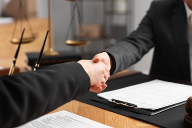 Photo of Notary shaking hands with client at wooden table in office, closeup