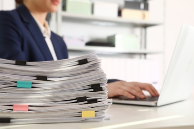 Photo of Stack of documents and woman working with laptop at table in office, closeup