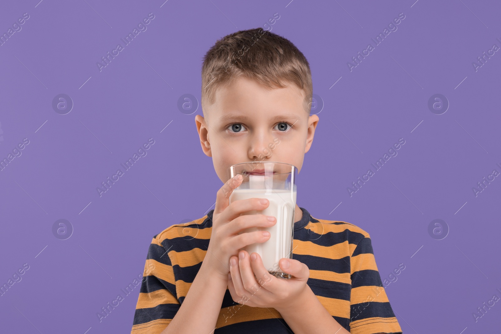 Photo of Cute boy with glass of fresh milk on violet background