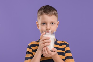 Cute boy with glass of fresh milk on violet background