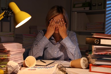 Overwhelmed woman surrounded by documents and paper coffee cups at table in office at night