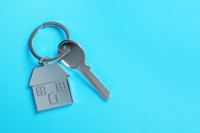 Photo of Key with keychain in shape of house on light blue background, top view. Space for text