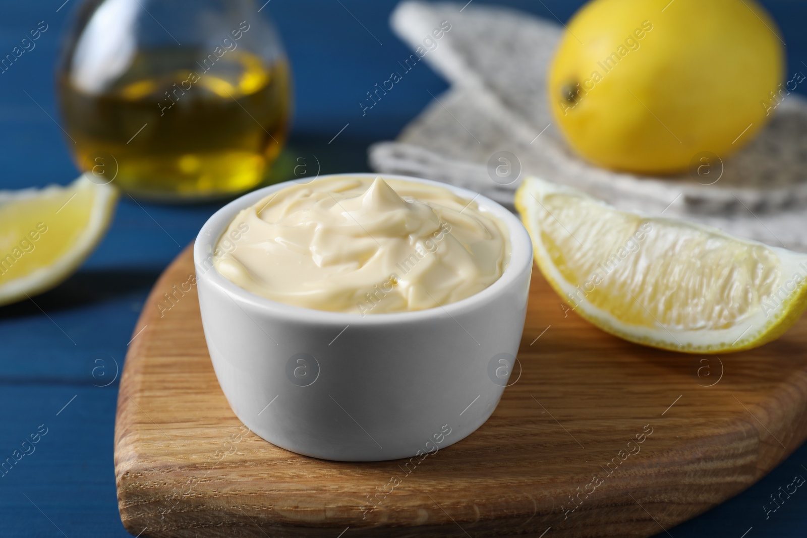 Photo of Tasty mayonnaise in bowl and lemon wedge on blue table, closeup