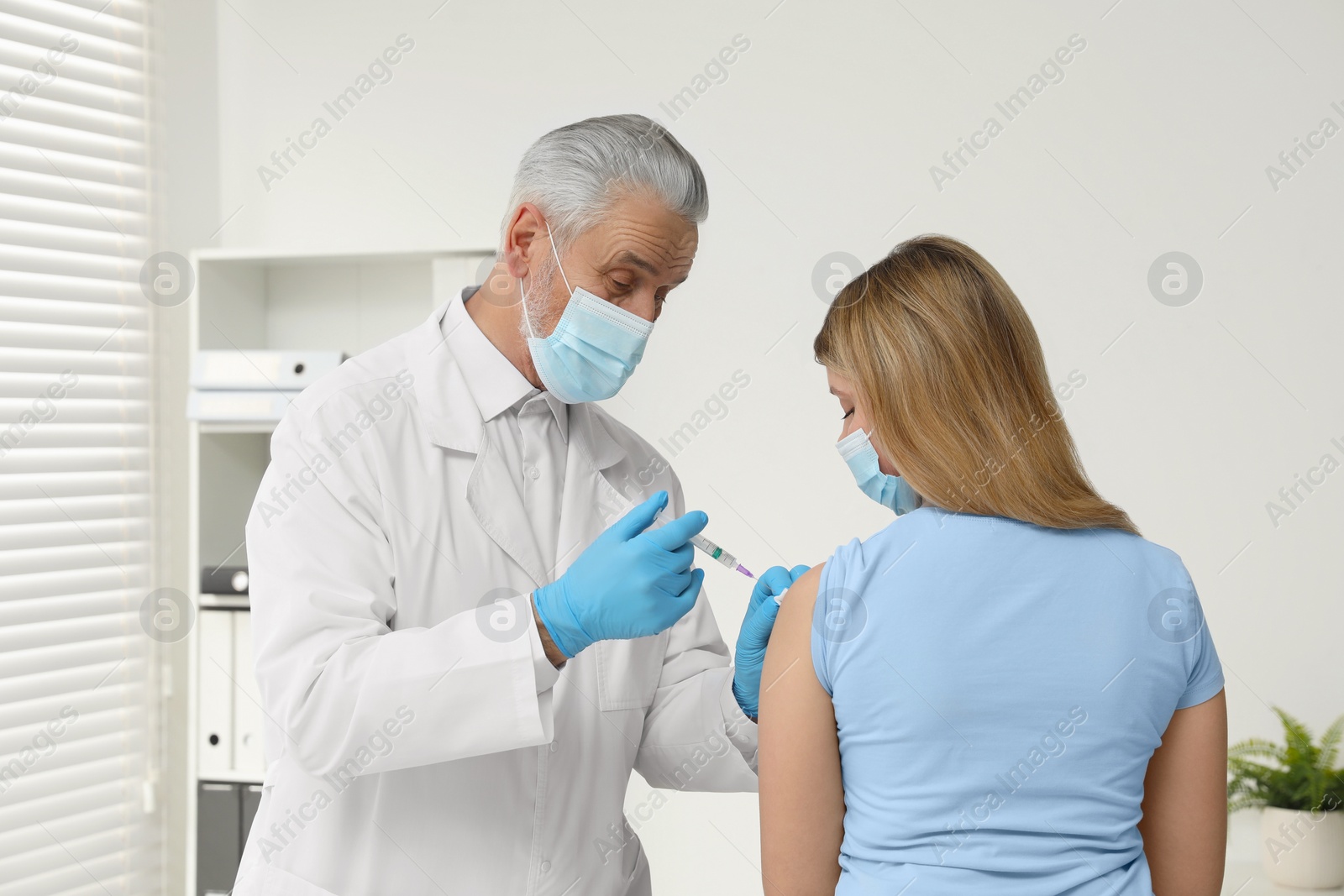 Photo of Doctor giving hepatitis vaccine to patient in clinic, back view