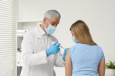 Doctor giving hepatitis vaccine to patient in clinic, back view