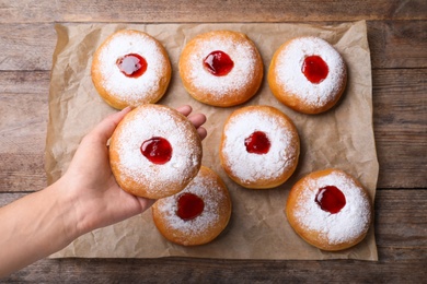 Photo of Woman holding Hanukkah doughnut with jelly and sugar powder over wooden table, top view