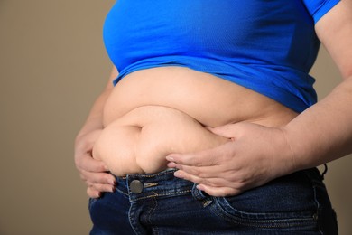 Overweight woman in tight shirt and jeans on light brown background, closeup