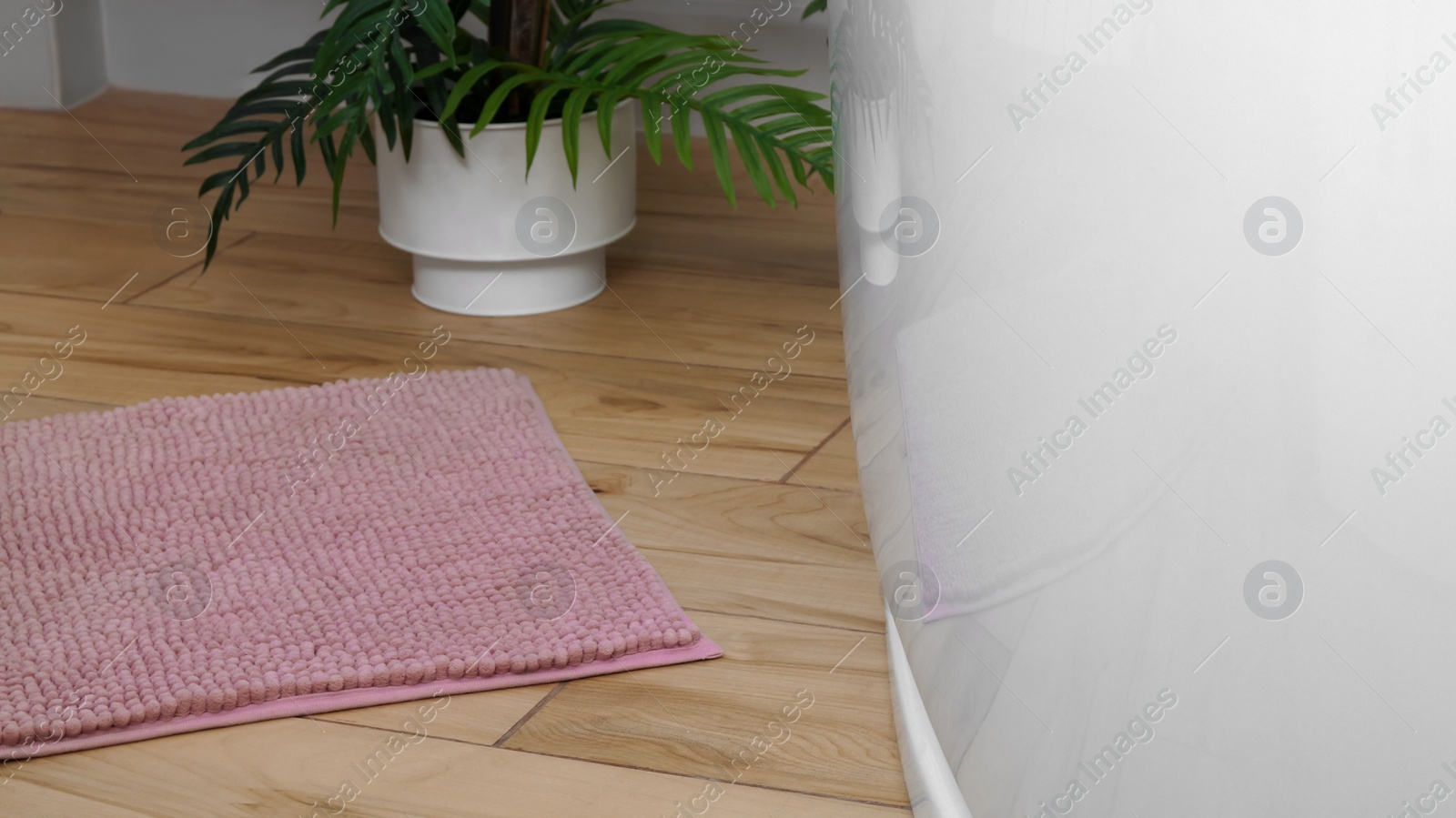 Photo of Pink mat near tub on wooden floor in bathroom