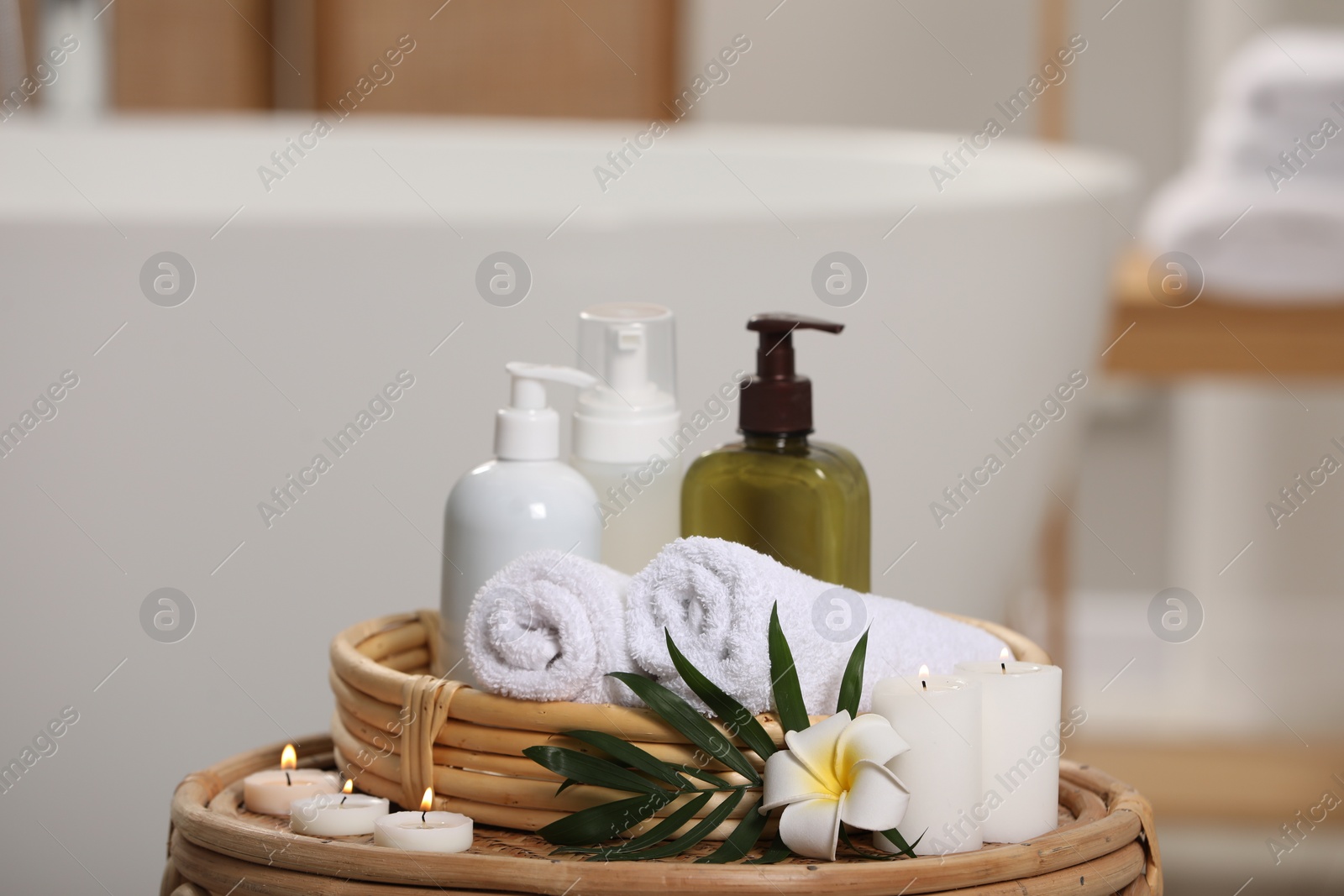 Photo of Spa products, burning candles, plumeria flower and tropical leaf on table in bathroom