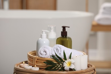 Spa products, burning candles, plumeria flower and tropical leaf on table in bathroom