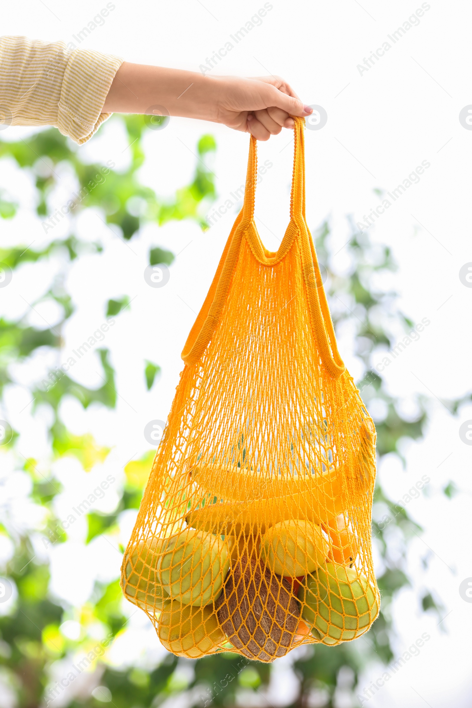 Photo of Woman with net bag full of fruits outdoors, closeup