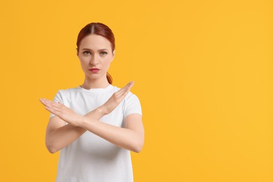 Photo of Stop gesture. Woman with crossed hands on yellow background, space for text