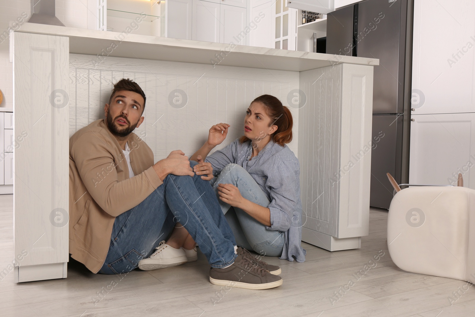 Photo of Scared couple hiding under table in kitchen during earthquake