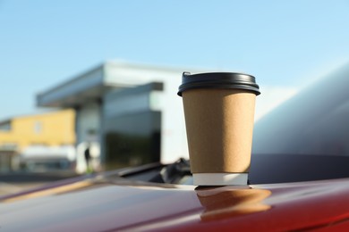 Photo of Paper coffee cup on car hood near gas station. Space for text