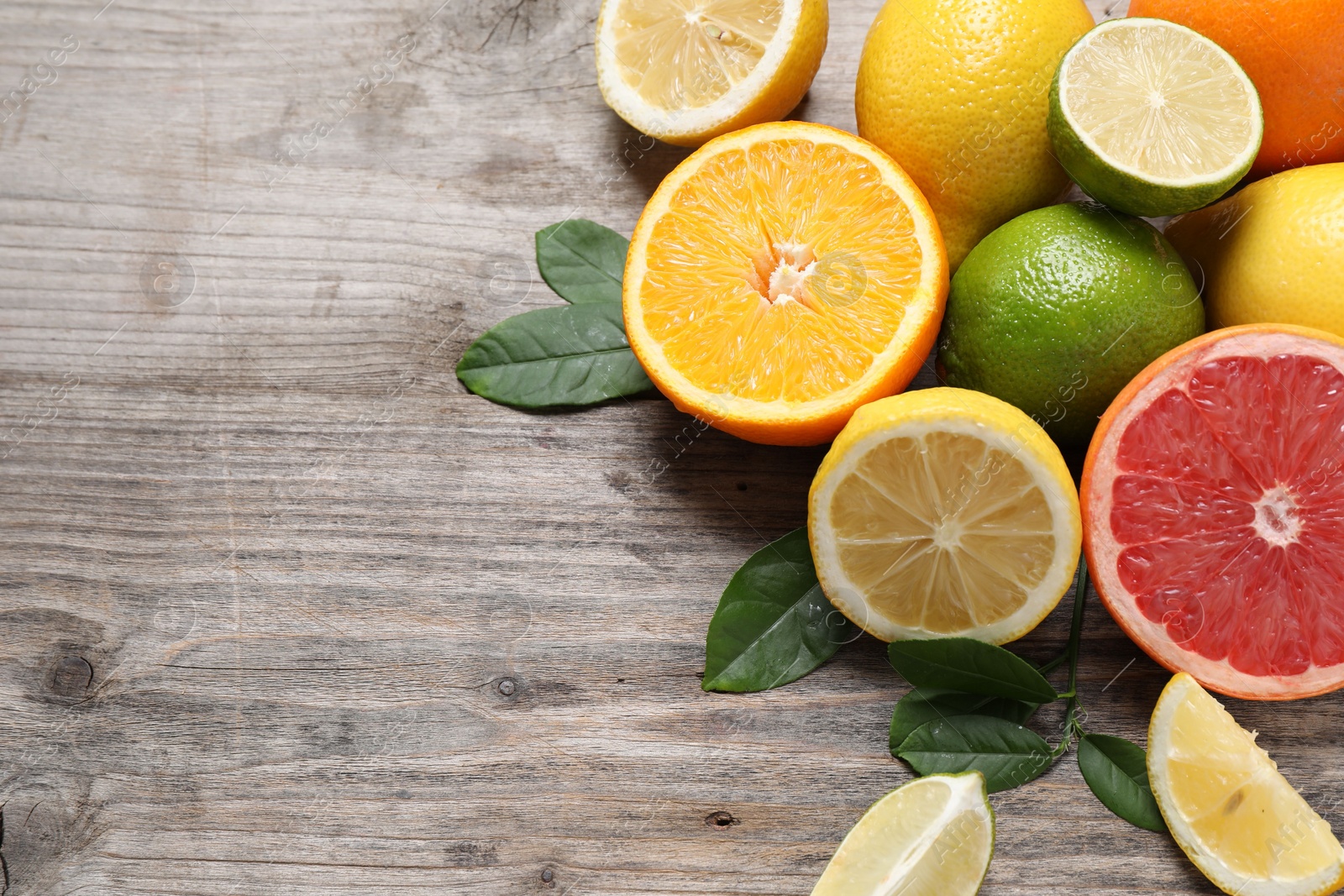 Photo of Different fresh citrus fruits and leaves on wooden table, flat lay. Space for text