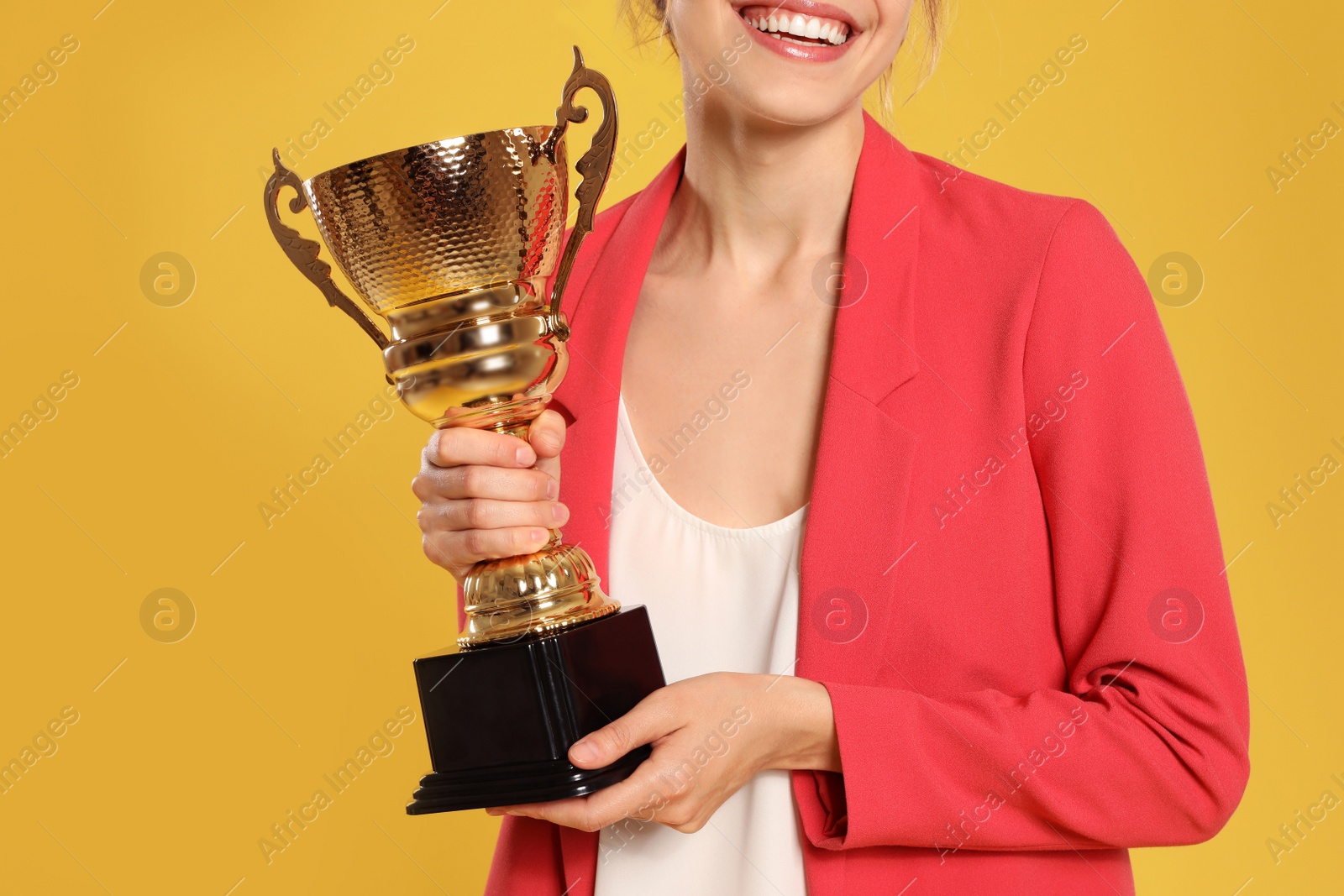 Photo of Young businesswoman with gold trophy cup on yellow background, closeup