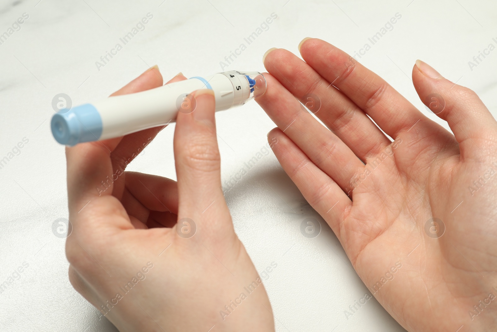 Photo of Diabetes. glucose testing. Woman using lancet pen at white marble table, closeup