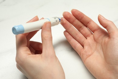 Photo of Diabetes. glucose testing. Woman using lancet pen at white marble table, closeup