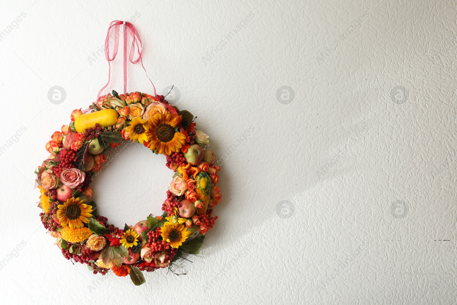 Photo of Beautiful autumnal wreath with flowers, berries and fruits hanging on white wall. Space for text