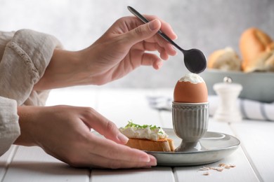 Photo of Woman eating fresh soft boiled egg at white wooden table, closeup