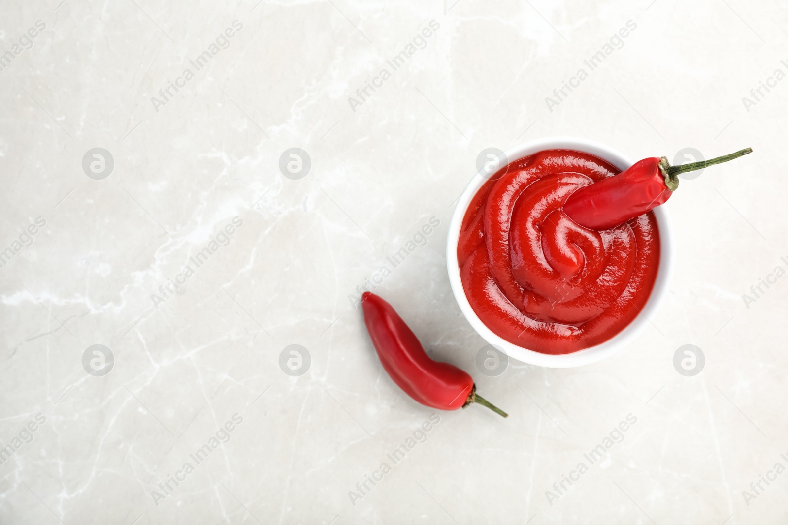 Photo of Bowl with spicy chili sauce and fresh peppers on light table, top view